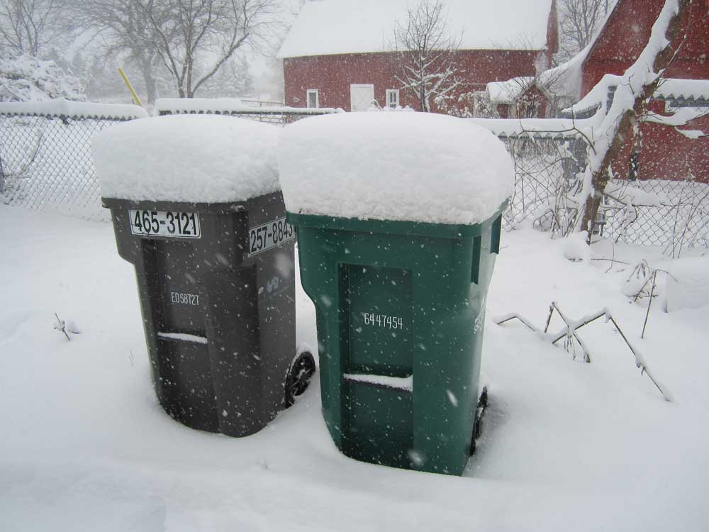 A foot of snow atop a garbage bin and a recycling bin.